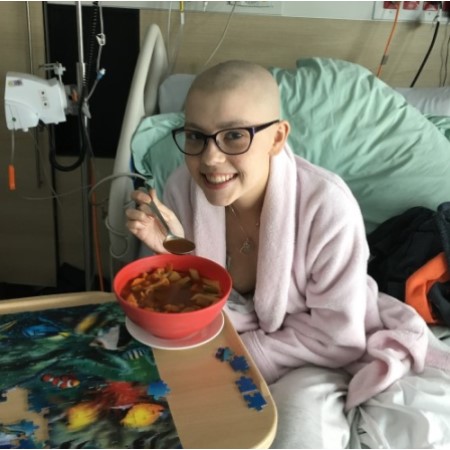 chelsea in hospital bed smiling and eating soup - help with a cancer donation