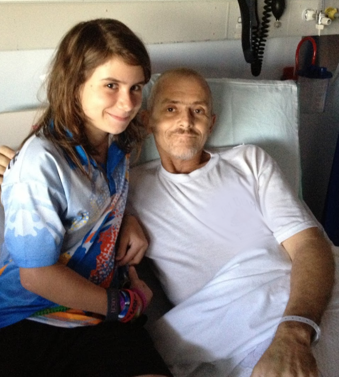 Chloe sitting on a hospital bed with her dad in a white tshirt 