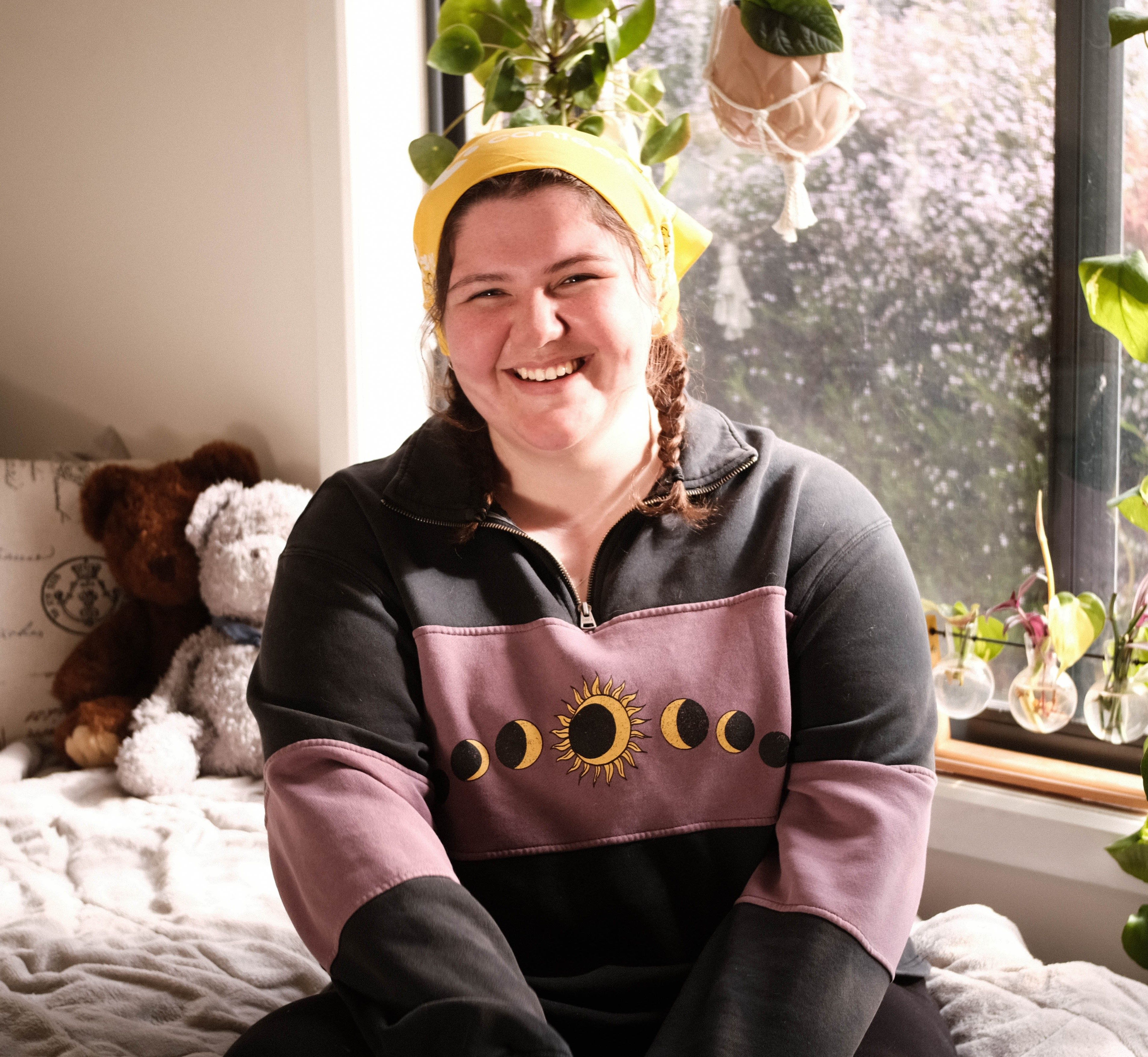 Tara, girl in early 20s, sitting on bed, smiling and wearing a yellow bandanna 